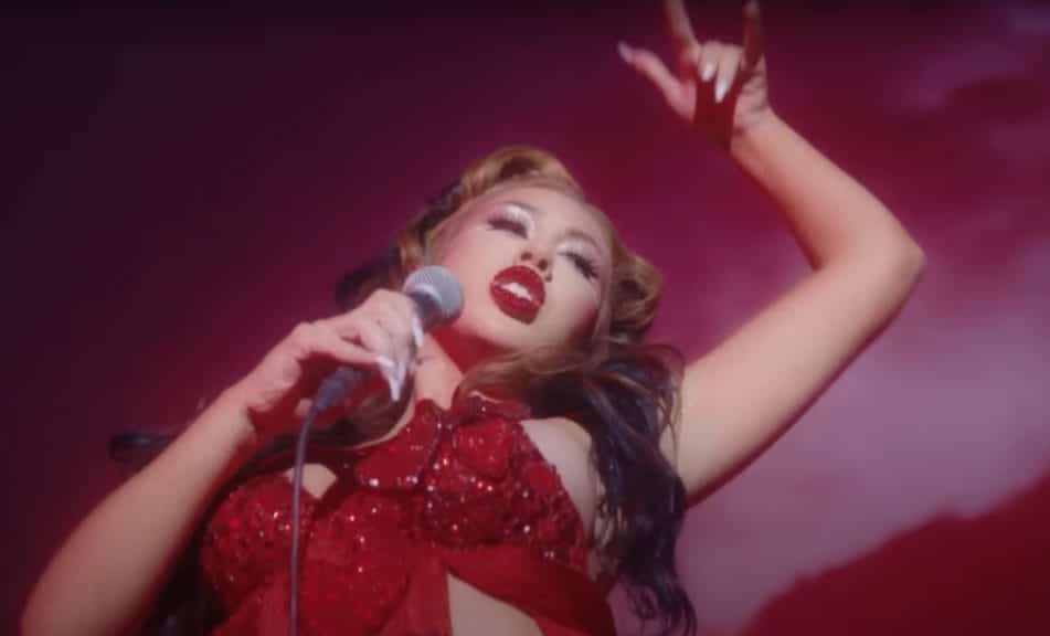 Kali Uchis in all red clothing, nail color, and red lips. She is dancing and singing with a microphone for 2021 music video for her song "telepatia"